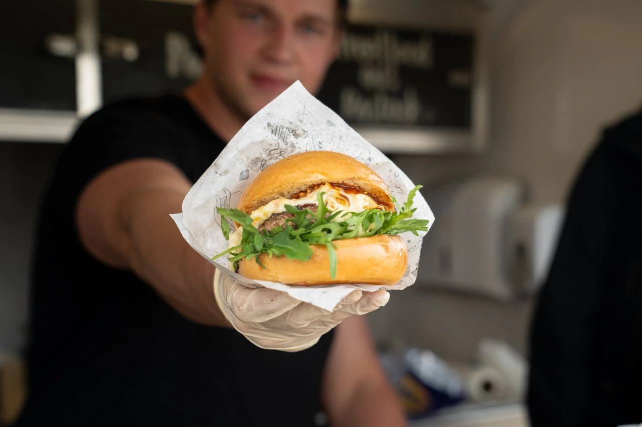 Ein Raclette-Burger wird mit ausgestreckter Hand gereicht